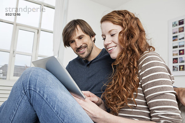 Germany  Munich  Couple sitting on sofa using digital tablet