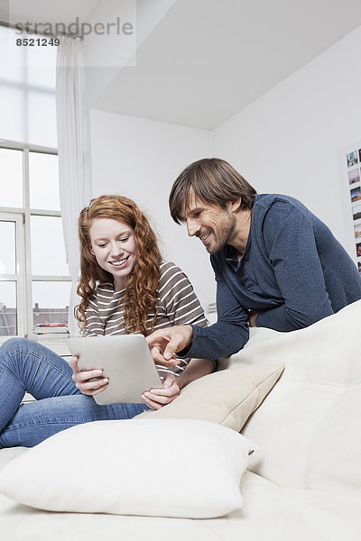 Deutschland  München  Paar sitzend auf Sofa mit digitalem Tablett