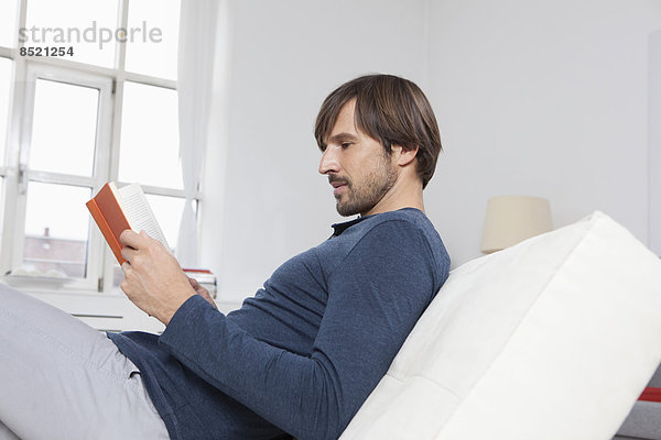 Mann auf Sofa sitzend  Lesebuch