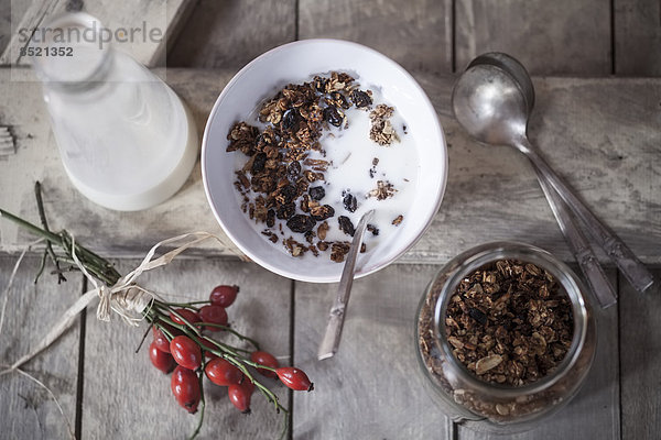 Bowl with granola made of baked oats  nuts and raisins  bottle of milk and rose hips on wooden board