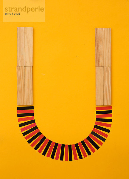 Buchstabe ''U'' aus Bausteinen und roten und schwarzen Papierstreifen auf gelbem Grund  Studioaufnahme'.