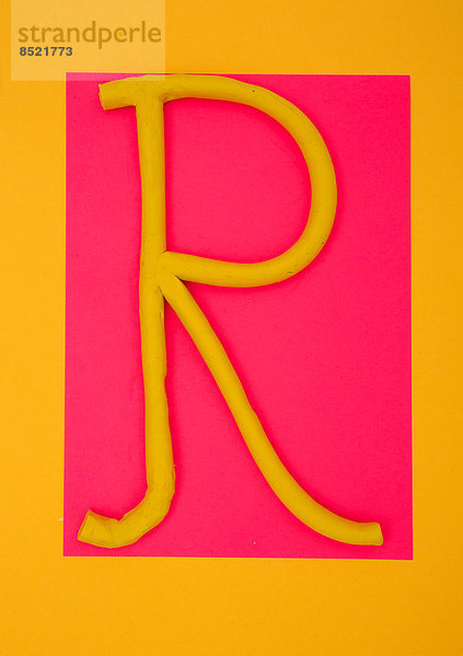 Buchstabe ''R'' aus Plastilin auf rosa und gelbem Grund  Studioaufnahme'.