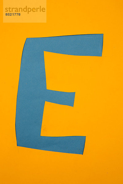 Buchstabe ''E'' aus blauem Papier auf gelbem Hintergrund  Studioaufnahme''.