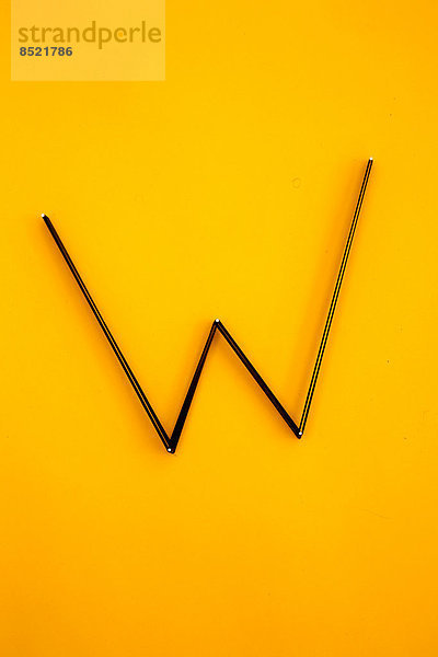 Buchstabe ''W'' aus Nägeln und Fäden auf gelbem Grund  Studioaufnahme'.