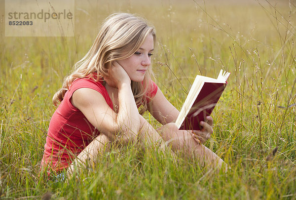 Austria  Salzkammergut  Mondsee  young woman reading book in a meadow