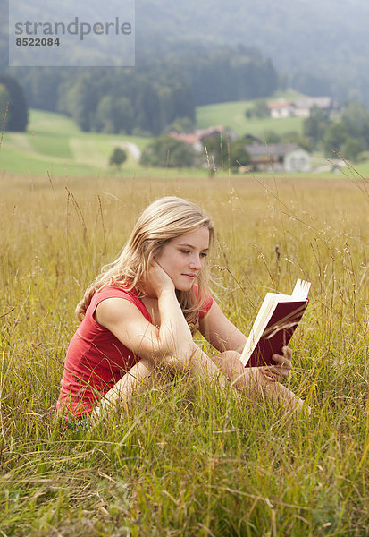 Österreich  Salzkammergut  Mondsee  junge Frau liest Buch auf einer Wiese