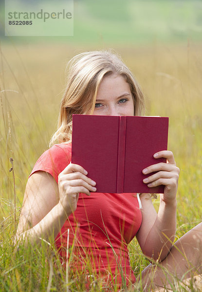 Österreich  Salzkammergut  Mondsee  junge Frau mit Buch auf einer Wiese sitzend