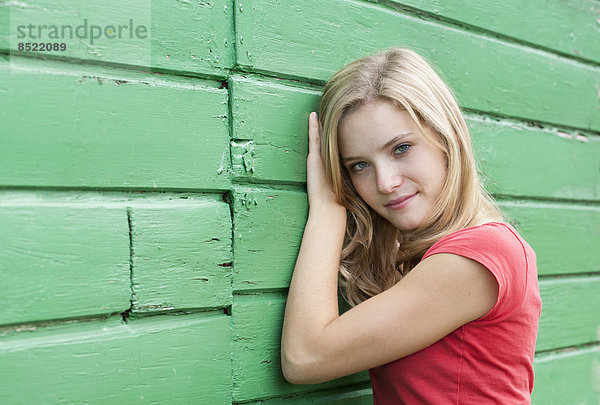 Österreich  Salzkammergut  Mondsee  Portrait einer jungen Frau  die sich an eine grüne Holzfassade lehnt