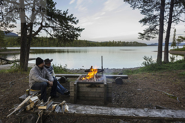 Paar sitzt vor Lagerfeuer auf dem Campingplatz der Insel Årrenjarka  Kvikkjokk  Norrbottens län  Schweden