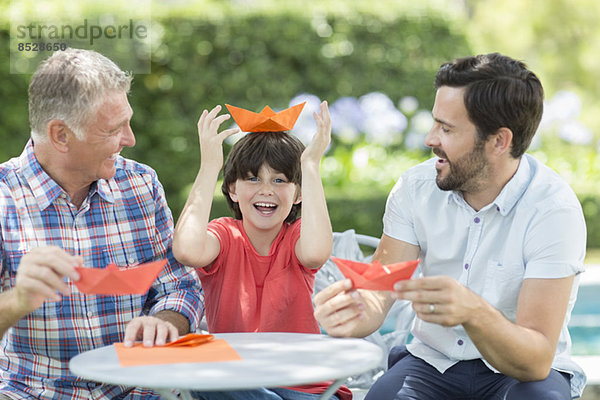 Mehrgenerationen-Männer machen Origami-Hüte im Freien