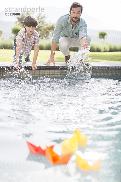 Vater und Sohn fahren Papierboote im Schwimmbad