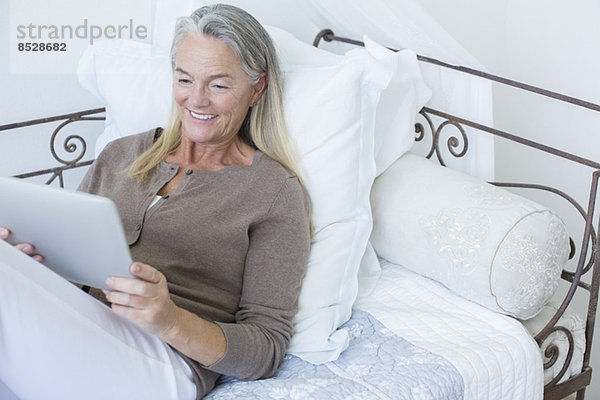 Seniorin mit digitalem Tablett auf dem Bett