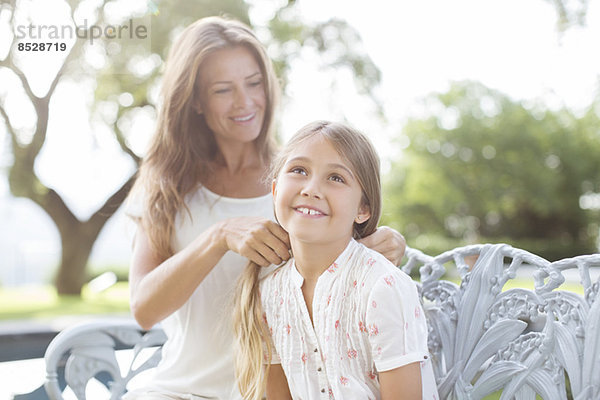 Mutter flechtet die Haare der Tochter im Freien.