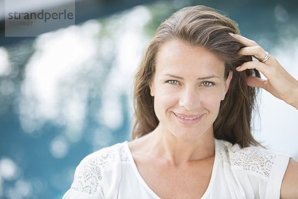 Frau lächelt mit der Hand in den Haaren am Beckenrand