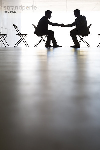 Silhouette von Geschäftsleuten  die im Büro die Hand schütteln