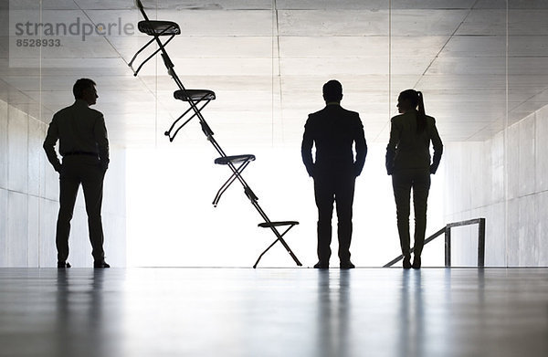 Geschäftsleute stehen neben Bürostuhl-Installationskunst