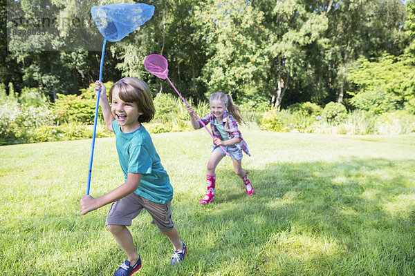 Junge und Mädchen rennen mit Schmetterlingsnetzen im Gras