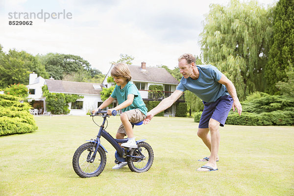 Vater schiebt Sohn auf Fahrrad im Garten