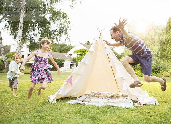 Vater jagt Kinder um das Tipi im Garten.