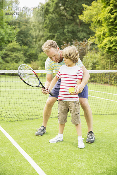 Vater lehrt den Sohn Tennis auf dem Rasen zu spielen.