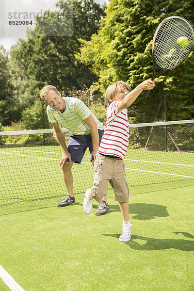 Vater und Sohn spielen Tennis auf Rasenplatz