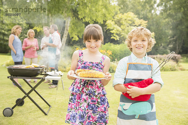 Bruder und Schwester halten gegrillten Mais beim Grillen im Garten