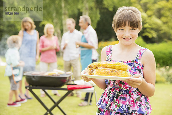 Lächelndes Mädchen mit gegrilltem Mais im Garten