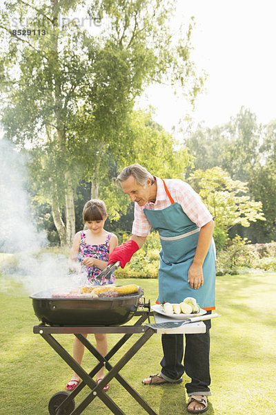 Großvater und Enkelin beim Grillen im Garten