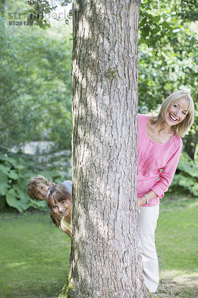 Großmutter und Enkelkinder blicken hinter den Baum