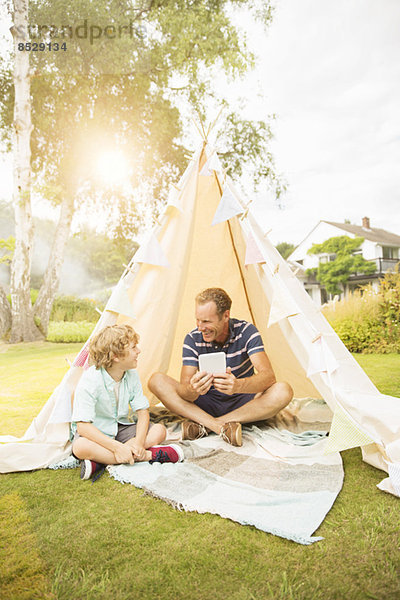 Vater und Sohn mit digitalem Tablett im Tipi im Garten