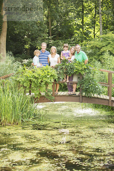 Mehrgenerationen-Familie auf Holzsteg über dem Teich stehend