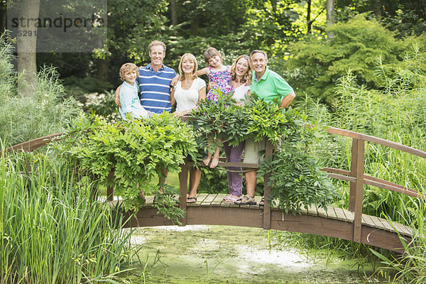 Mehrgenerationen-Familie auf Holzsteg über dem Teich stehend