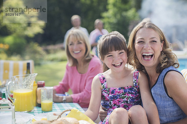 Mehrgenerationen-Familie lacht bei Tisch im Hinterhof