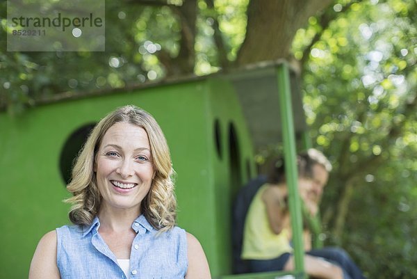 Frau lächelt mit Baumhaus im Hintergrund