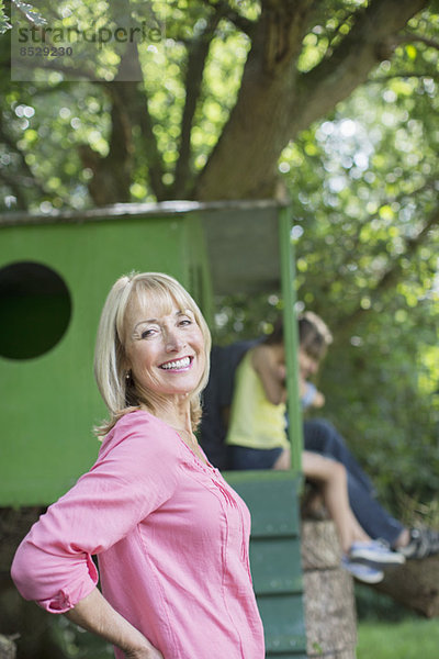 Frau lächelt mit Baumhaus im Hintergrund