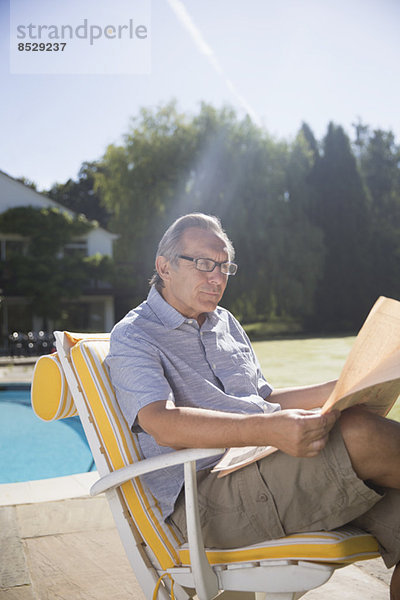 Mann liest Zeitung am Pool