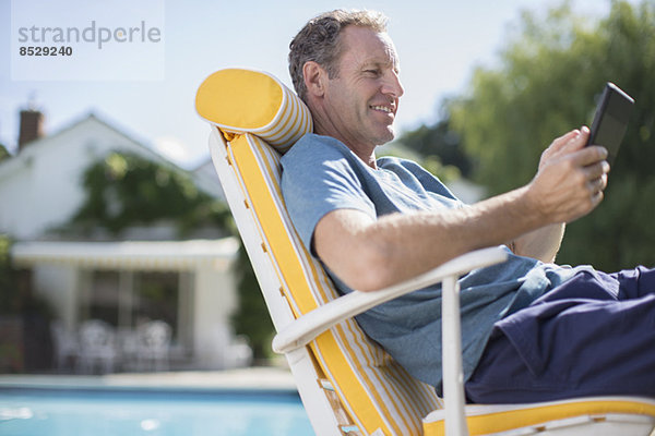 Mann liest im Sessel am Pool