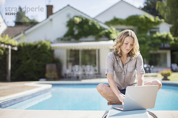 Frau mit Laptop am Sprungbrett am Pool