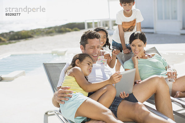 Familie mit digitalem Tablett auf dem Liegestuhl am Pool