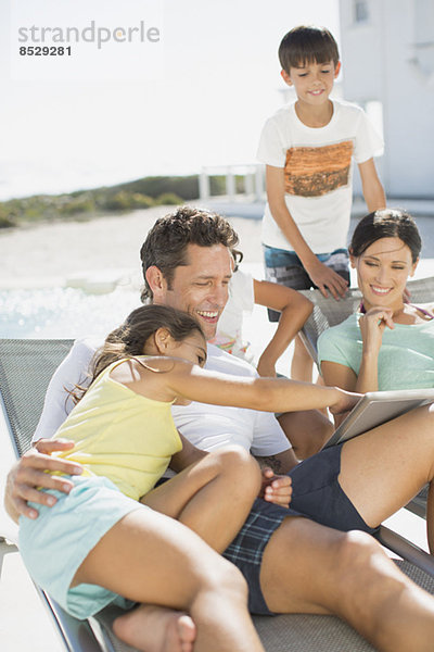 Familie mit digitalem Tablett auf Liegestühlen am Pool