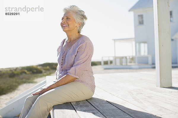 Seniorin auf Deck vor dem Strandhaus sitzend