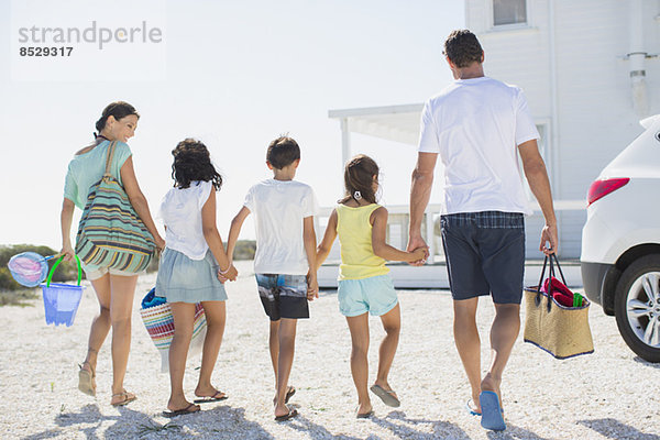 Familie hält sich an den Händen und trägt Strandkleidung in der sonnigen Einfahrt.
