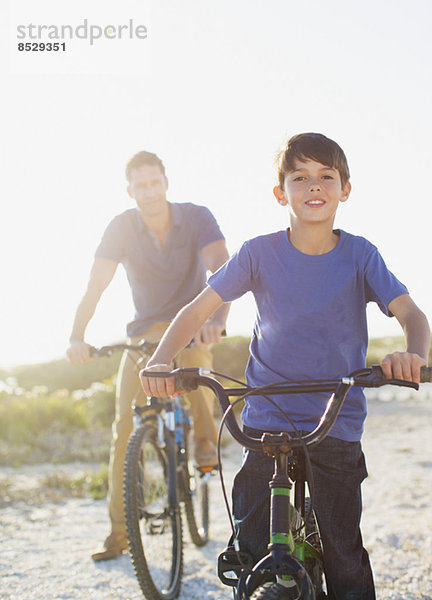 Vater und Sohn beim Fahrradfahren am sonnigen Strand