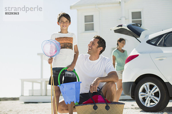 Vater und Sohn halten Strandkleidung vor dem Auto in der sonnigen Einfahrt.