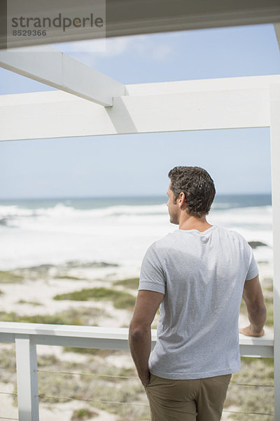 Mann blickt vom Balkon auf das Meer