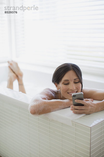 Frau mit Handy in der Badewanne