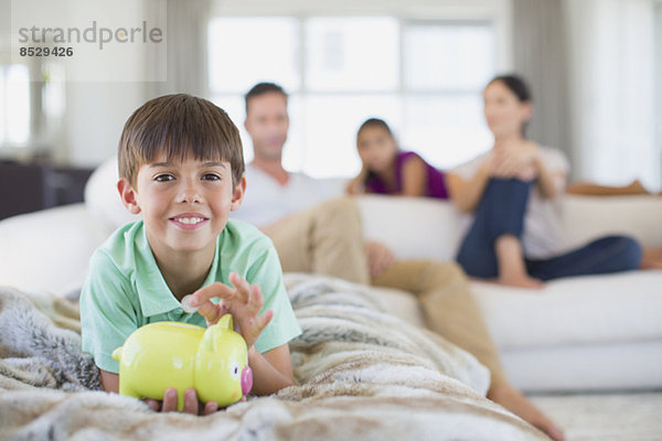 Junge mit Sparschwein auf Sofa im Wohnzimmer