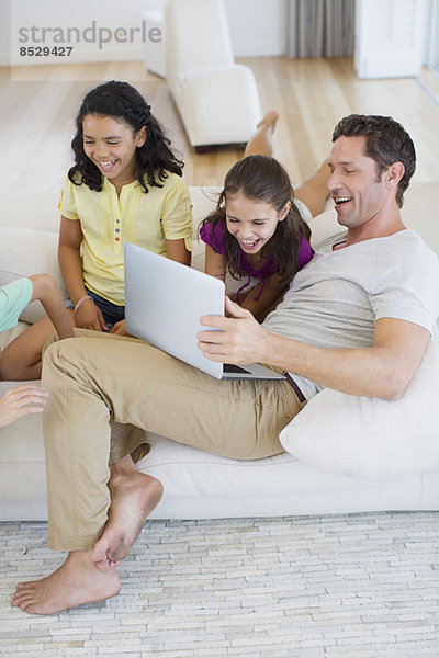 Vater und Töchter mit Laptop auf Sofa im Wohnzimmer