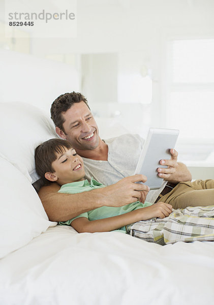 Vater und Sohn mit digitalem Tablett auf dem Bett