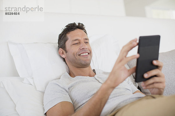 Mann mit digitalem Tablett im Bett